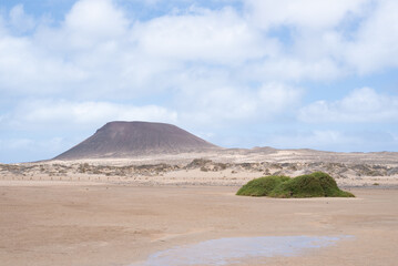 View of one of the volcanoes of La Graciosa, the eighth Canary Island. Golden sand and crystal clear water in a desertic landscape.