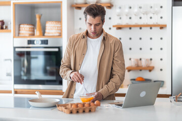 A male freelancer beat eggs in a bowl and made scrambled eggs in the kitchen.