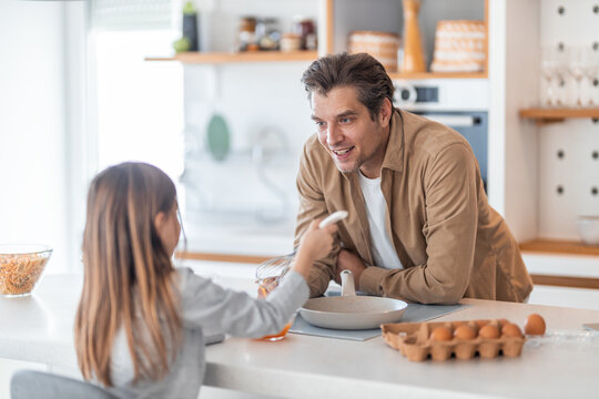 A caring father watching his cute girl beating yolks for a breakfast meal.
