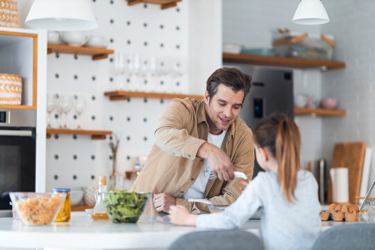 A father gives his daughter a kitchen tool for beating eggs and making breakfast.