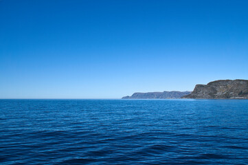 View from the sea to the West Cape in Norway in sunshine. Waves and rocks