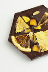 Handmade dark chocolate bar with a dried fruit topping - slices of orange, mango, pineapple. Homemade Chocolate bark in shape of honeycomb. Top view. Isolated on white background. Copy space