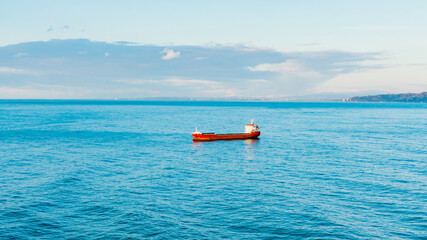 A lone ship is anchored near the seaport in the bay at sunset, aerial view