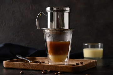 Cooking traditional Vietnamese coffee with condensed milk in glass cup on black background. Close up.