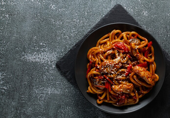 Udon stir-fry noodles with chicken and vegetables on stone background, top view.