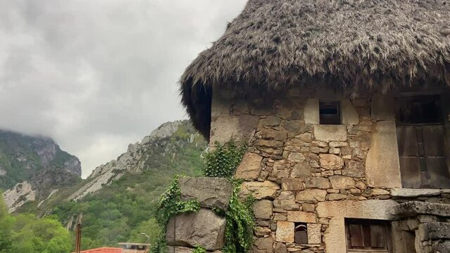 Close-up of an old stone hut with thatched roof in the middle of a green valley on a cloudy day