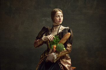 Portrait of young beautiful girl, princess in vintage, elegant costume with baguette and vegetables...