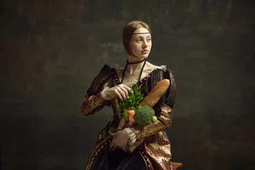 Tapeten Portrait of young beautiful girl, princess in vintage, elegant costume with baguette and vegetables on dark green background. Concept of history, renaissance art, comparison of eras. Grocery shopping © master1305