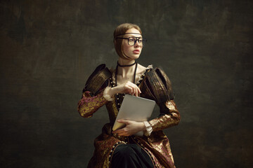 Portrait of young, pretty girl, royal person in vintage dress and modern glasses posing with laptop...
