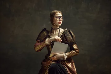 Tapeten Portrait of young, pretty girl, royal person in vintage dress and modern glasses posing with laptop against dark green background. Business woman. History, renaissance art, comparison of eras concept © master1305