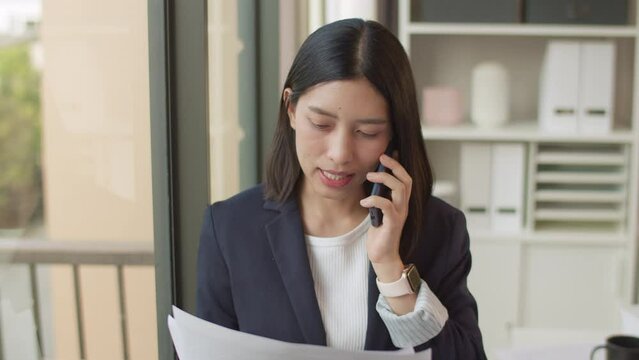 Positive Asian businesswoman talking smartphone in office.