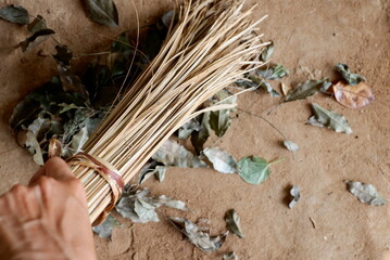 Left hand holding Coconut stalks tied together sweep the leaves on the ground