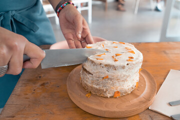 Waiter slicing a tasty homemade carrot cake with knife to serve into a cafeteria.