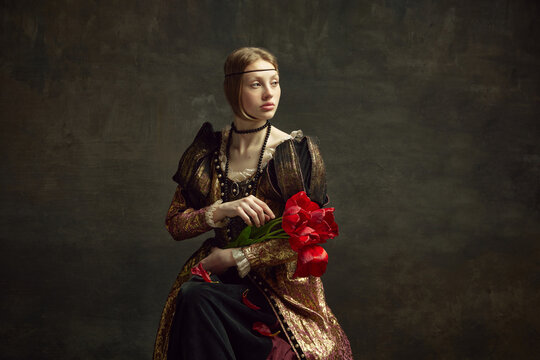 Portrait of beautiful young girl, royal person, queen in elegant vintage dress posing with flowers, tulips against dark green background. Concept of history, renaissance art remake, comparison of eras