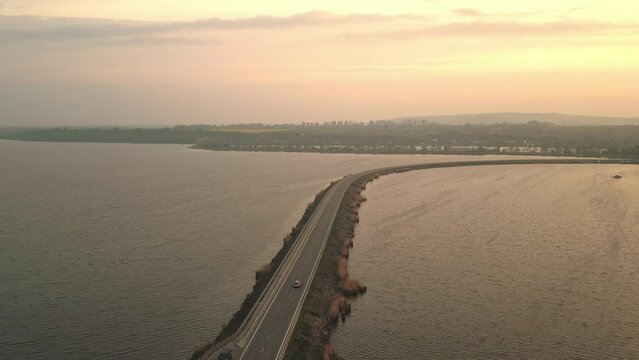 The sun setting over the road running down the middle of the dam, with a car driving along it.