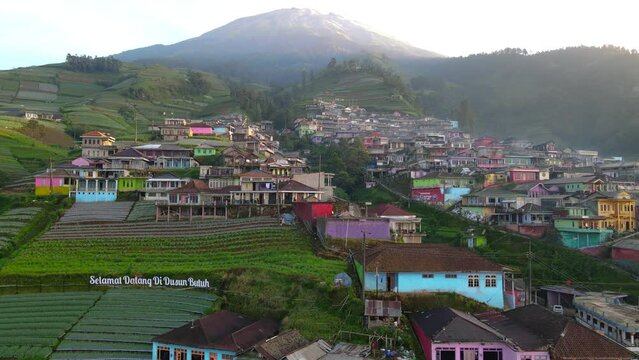 Drone View : Beautiful view of Nepal Van Java with text "Selamat Datang di Dusun Butuh" or "Welcome to Butuh Village" installed at the entrance in clear weather - 4K aerial video
