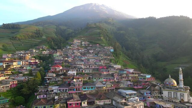 Fly over Dusun Butuh or Nepal Van Java on the slope of Mount Sumbing. Colorful terraced house of village with peak of mountain visible. Mount Sumbing climbing post - 4K aerial view
