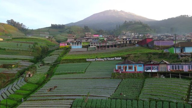 Fly over entrance of Nepal Van Java Village with text "Selamat Datang di Dusun Butuh" or "Welcome to Butuh Village". Mount Sumbing climbing post - 4K Aerial drone shot