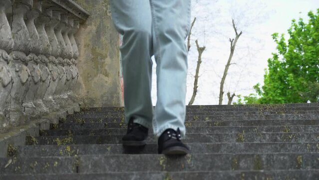 Woman legs in jeans walking on ancient stair front view. Female foot in black suede shoe go down step by step on old classic balustrade. Feet coming and climbing down Disrupted stair and stone railing