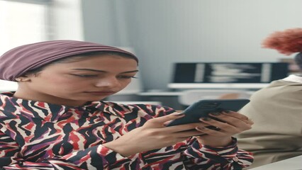 Vertical shot of young Muslim woman using smartphone while working with multiethnic programmers in bright office - Powered by Adobe