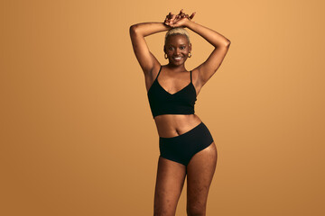 Cheerful black woman in underwear with raised arms in studio