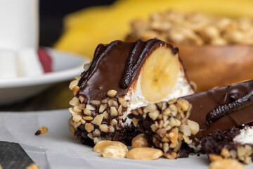 Sliced sweet cake with banana, chocolate glaze, milk filling and peanuts