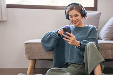 Happy asian woman listening to music from mobile phone while sitting near sofa at homes, Smiling...