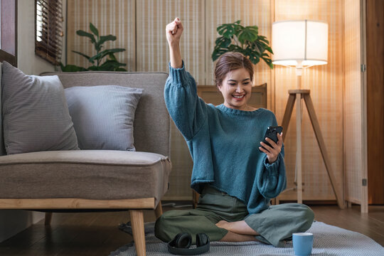 Happy asian woman listening to music from mobile phone while sitting near sofa at homes, Smiling girl relaxing with headphones in morning, Time to relax. copy space.