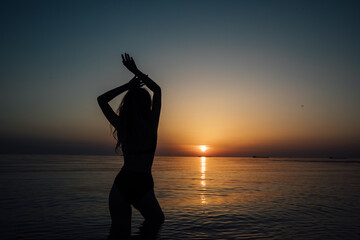 silhouette of a woman in a swimsuit on the beach at sunset by the sea walk rest