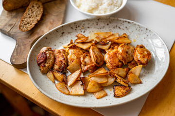 Quail breast with roasted sliced pear on plate, rice in bowl, bread on cutting board .