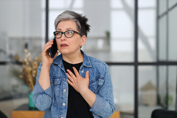 Shocked mature woman talking on mobile phone, unexpected news.