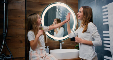 Caucasian young and child sisters brushing teeth looking at each other smiling. Smilling woman and...