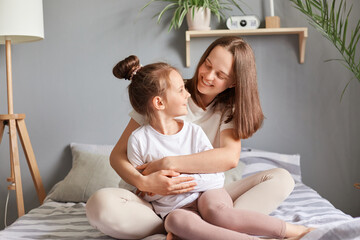 Smiling adult woman embraces her cute little girl in their beautiful bedroom, enjoying moment of...