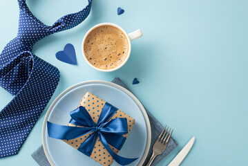 Make Father's Day extra special with a delightful table setting. Flat lay top view of plates, coffee, cutlery, napkin, giftbox, necktie on a pastel blue background with a blank space for text or ad