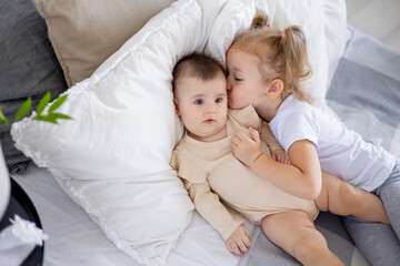 older sister baby kisses and hugs baby at home on the bed, love and friendship of sisters in the family