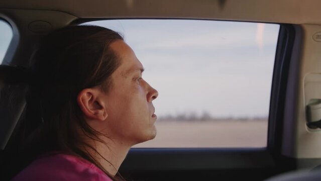 Profile portrait of young man with long hair in car. Handheld pov shot of camera