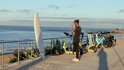 Young handsome asian man getting the new surfboard. he takes photo or pics to share on instagram or facebook with some waves crashing in background.