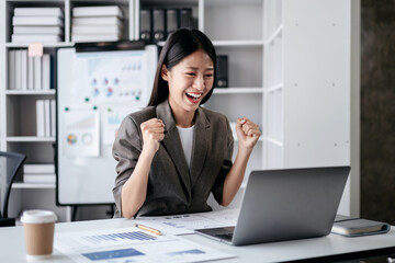 Accounting business concept, Accountant woman reads good news on laptop with excited and raising fist to celebrate achievement while working about investment with business planning finance