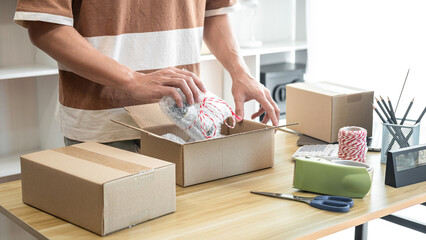 Male entrepreneur is packing the product into cardboard boxes fo
