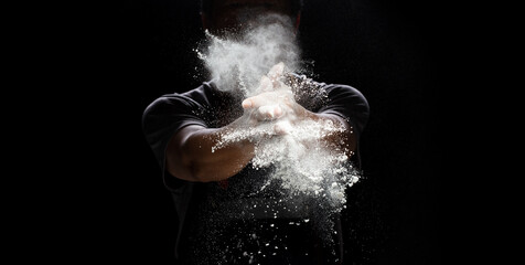Chef prepare white flour dust for cooking bakery food. Elderly man Chef clap hand, white flour dust explode fly in air. Flour stop motion in air with freeze high speed shutter, black background