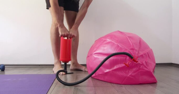 Man inflating fitness ball using hand pump at home, 