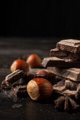 Close-up of hazelnuts with aniseed chocolate pieces, selective focus, on wooden table, black background, vertical, with copy space