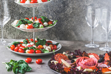 Classic Italian salad Insalata Caprese and a plate with a selection of sausage specialties on gray background