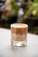 Dirty Coffee, in a clear glass, placed on the table. There is bokeh of trees in the background.