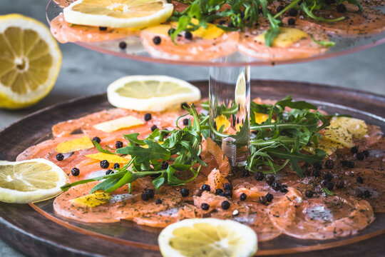 Salmon carpaccio with lemon and rocket on a cake stand, italian starter, antipasti, gray background, close up.