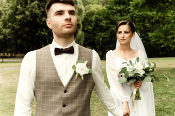 a handsome groom holds the hand of a beautiful bride by the hand while in the park. wedding...