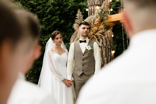 wedding ceremony in the park. newlyweds on the background of a wedding wooden arch in rustic style. vow exchange. pastor crowns