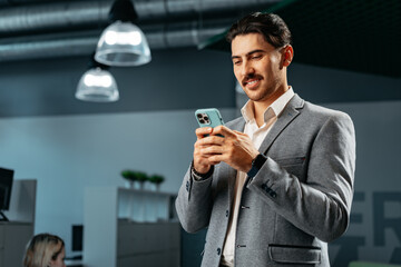 Handsome young arab man in formal wear using smartphone in office