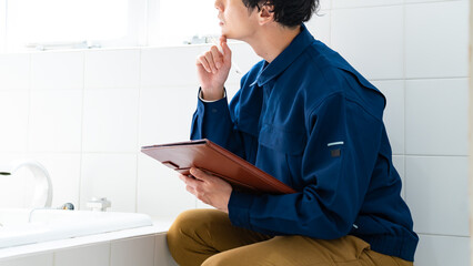 風呂場をチェックする作業着を着た日本人男性