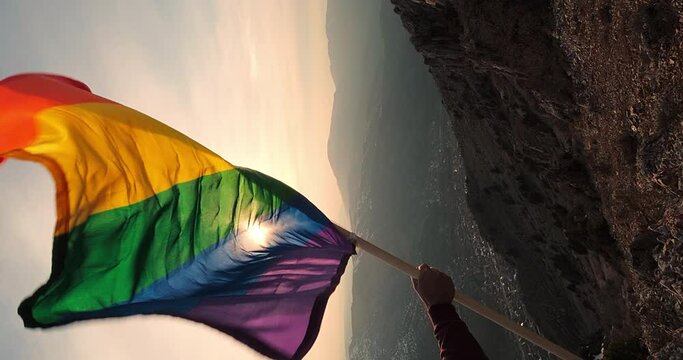 Male Hand Holding Pride Flag Waving Against the Wind, of Symbolizing the Support for Human Rights in Their Regard. LGBT Flag Set Up on the Peak of Mountain. Vertical Video. Copy Space for Place a Text